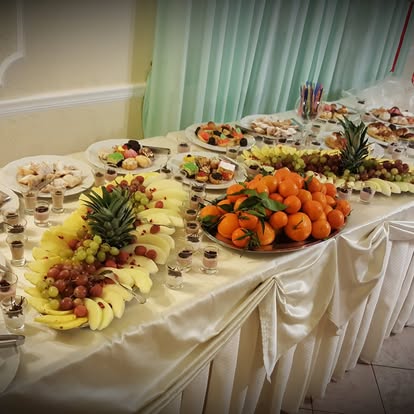 Buffet di frutta con ananas, arance, uva e banane accanto ai dolci in bicchierini