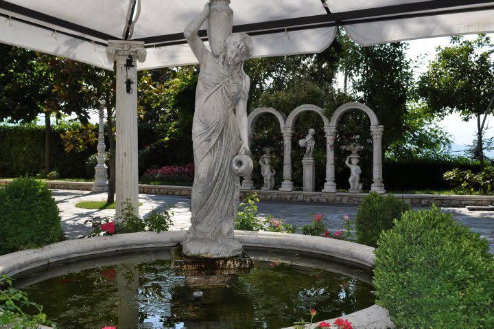 Statua con anfora al centro di una fontana sotto il gazebo, con gli archi bianchi e le statue sullo sfondo
