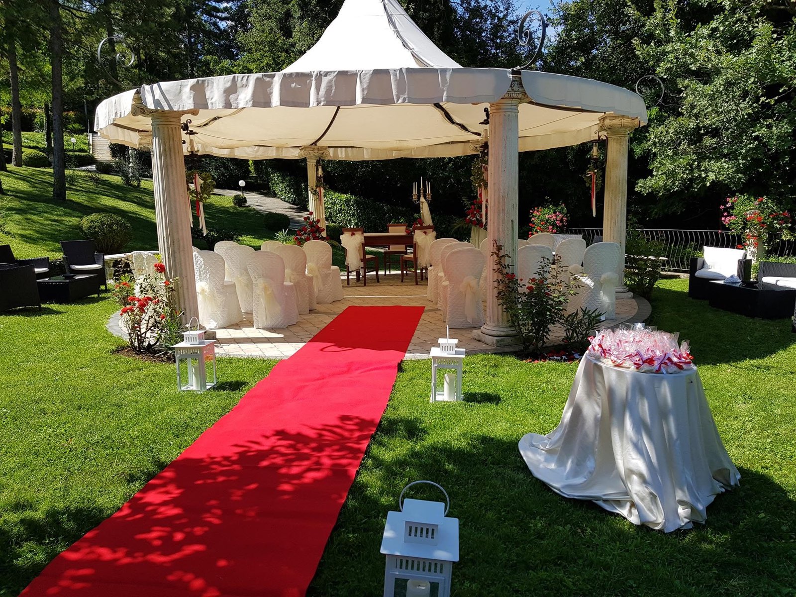 Il gazebo bianco in giardino allestito per una cerimonia, con tappeto rosso, lanterne e sedie rivestite