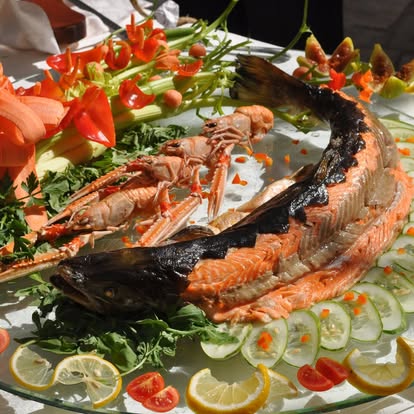 Salmone intero con scampi, limoni, pomodorini e verdure su un vassoio di vetro