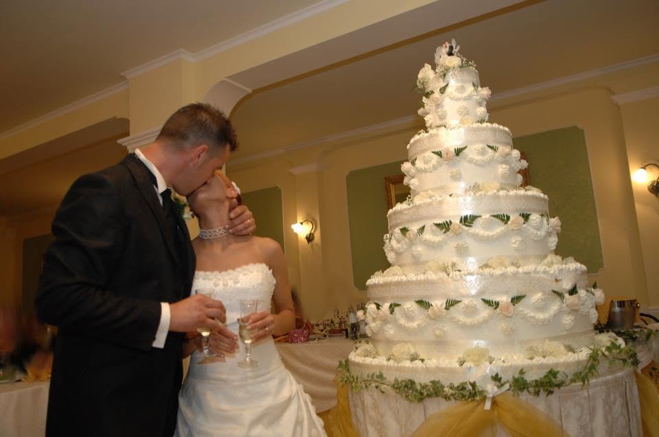 Gli sposi si baciano accanto a una grande torta nuziale a più piani in sala